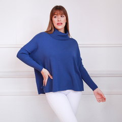 Modelo luciendo un polerón marina de color azul con cuello alto, combinado con pantalones blancos.