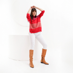 Modelo usando una polera Rina de rayas rojas y rosas, combinada con pantalones blancos y botas marrones.