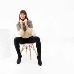 Modelo luciendo la polera Yursula de color beige con detalles a cuadros, sentada en una silla blanca.