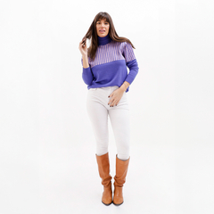 Modelo usando una polera Yursula de color púrpura con detalles en rosa, combinada con pantalones blancos y botas marrones.