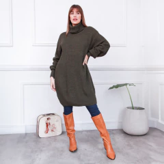 Modelo luciendo un polerón Clara de color verde oliva, con botas altas naranjas y jeans, en un ambiente moderno y minimalista.
