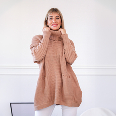 Modelo sonriente usando un polerón Zoe de color nude, con cuello alto y bolsillos, en un ambiente luminoso y minimalista.