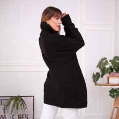 Modelo usando un polerón negro de cuello alto, en un entorno minimalista con plantas decorativas.