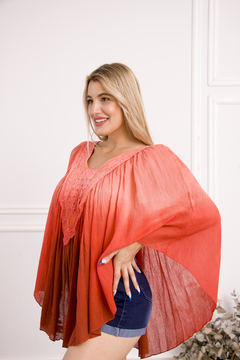 Poncho Amaru color coral con detalles de encaje, usado por una mujer sonriente, en un fondo neutro.
