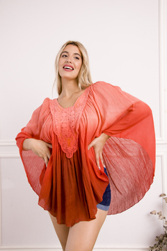Poncho Amaru de bambula, color coral, con detalles de guipur en el escote, lucido por una modelo en un fondo neutro.