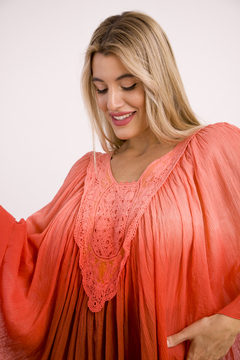 Poncho Amaru en color coral, con detalles de encaje en el escote y caída amplia, modelado por una mujer sonriente.