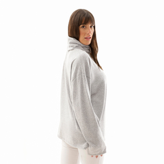 Poncho polera gris, con cuello alto, usado por una mujer de perfil, destacando su diseño cómodo y moderno.