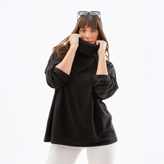 Poncho polera negro con cuello alto, modelo femenino con cabello largo y lacio, posando con las manos en el cuello.