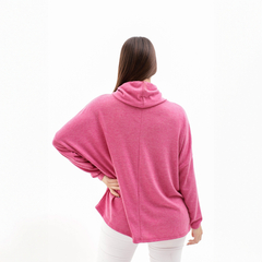 Vista trasera de un poncho polera rosa, con un diseño holgado y un cuello alto, usado por una mujer de cabello largo.