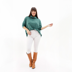 Poncho polera verde con cuello, modelo femenino posando con pantalones blancos y botas marrones.