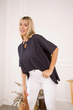 Modelo luciendo una remera negra con un detalle en el cuello, combinada con pantalones blancos y un bolso.