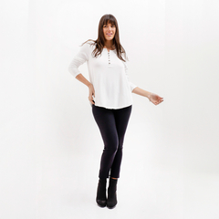 Modelo luciendo una remera blanca de manga larga con botones, combinada con pantalones oscuros y botas negras.