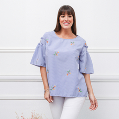 Remera Kaia de rayas azul con flores bordadas, con mangas amplias, modelo posando en un fondo blanco.