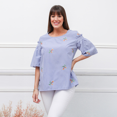 Remera Kaia de rayas azules con bordados coloridos, modelo femenino posando con una mano en la cadera.