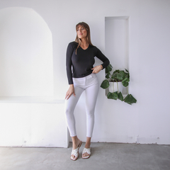 Modelo posando con remera negra de manga larga y pantalones blancos en un ambiente minimalista.
