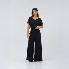 Modelo luciendo una remera negra con pantalones anchos en un fondo blanco.