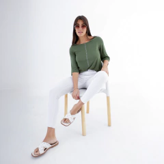 Mujer sentada en una silla, vistiendo una remera verde y pantalones blancos, con gafas de sol y sandalias blancas.