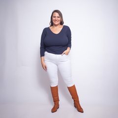 Mujer sonriente usando una remera de color azul oscuro y pantalones blancos, con botas marrones.