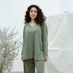 Remerón Vica en color verde, modelo con cabello rizado posando frente a una pared blanca y una planta seca al lado.