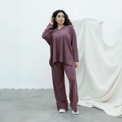 Modelo vistiendo un remerón y pantalones de color púrpura, en un ambiente minimalista.