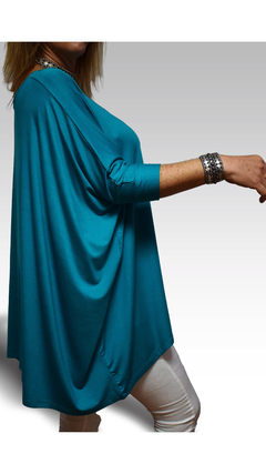 Remerón Alma Largo de color turquesa, con mangas largas y un diseño holgado, modelado por una mujer. Se aprecian accesorios en la muñeca y un fondo suave.