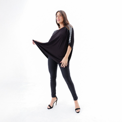 Mujer posando con una blusa negra de Remeron Amu y pantalones ajustados oscuros en un fondo blanco.