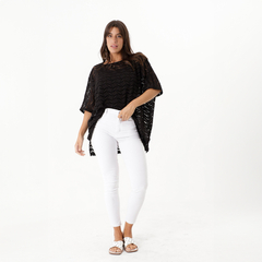 Modelo luciendo un remerón de crochet negro con pantalones blancos ajustados y sandalias blancas.