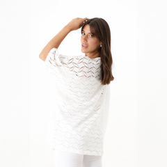 Modelo luciendo un remerón de crochet blanco con diseño de calados, girando hacia un lado y sonriendo.