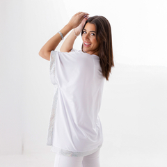 Modelo luciendo una remera blanca con detalles brillantes en los bordes, sonriendo mientras se gira hacia atrás.