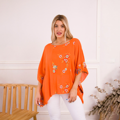 Remerón naranja con bordados florales, modelo luciendo la prenda en un entorno luminoso.