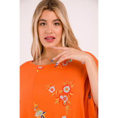 Modelo luciendo un remerón naranja con bordados florales en un fondo neutro.