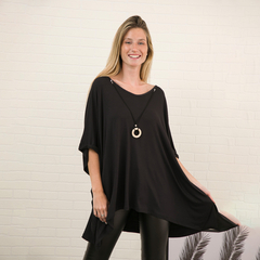 Modelo luciendo un remerón negro llamado Indiana, con un collar decorativo, en un fondo de pared blanca.