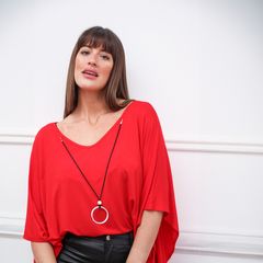Mujer luciendo un reméron rojo con un collar negro y detalle plateado, frente a un fondo blanco.