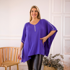 Remerón Indica de color púrpura, con detalles brillantes en las mangas y un diseño suelto, modelado por una mujer sonriente en un ambiente elegante.