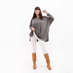 Remerón López de color gris, con una mujer posando en un fondo blanco, usando pantalones blancos y botas marrones.