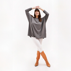 Modelo usando un remerón gris con mangas largas, combinado con pantalones blancos y botas de caña alta color naranja.