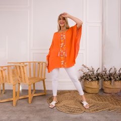 Remerón naranja con bordados florales, usado por una modelo en un ambiente moderno.