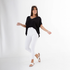 Mujer posando con una blusa negra y pantalones blancos, mostrando un estilo moderno y casual.