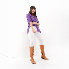 Mujer posando con un suéter morado y pantalones blancos, usando botas altas marrones.