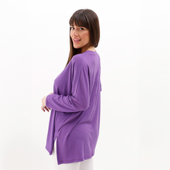 Mujer posando de perfil con una blusa morada de manga larga.