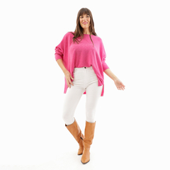 Modelo posando con un remerón rosa brillante, combinado con jeans blancos y botas marrones.