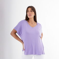 Modelo usando una blusa morada con detalles decorativos en el escote y los laterales.