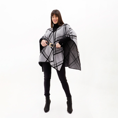 Una mujer usando una ruana con diseño a cuadros en tonos gris y negro, combinada con un suéter negro y pantalones oscuros.