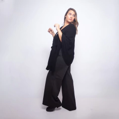 Mujer de pie usando una ruana negra llamada Ruana Batilde combinada con pantalones oscuros y zapatos negros, fondo blanco