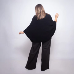 Mujer de espaldas vistiendo una ruana negra amplia y pantalones oscuros de vestir en fondo blanco