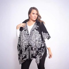 Mujer usando ruana negra con diseño de flores blancas grandes, sobre camisa blanca y pantalón negro