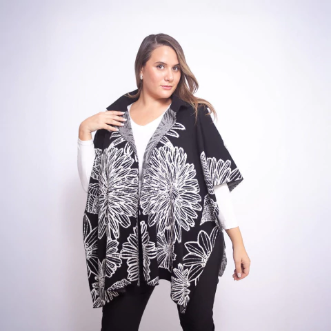 Mujer usando ruana negra con diseño de flores blancas grandes, sobre camisa blanca y pantalón negro