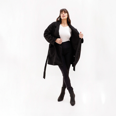 Mujer posando con abrigo negro y pantalones oscuros, mostrando un look moderno y elegante.