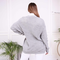 Mujer de espaldas usando un saco inglés gris, con cabello largo y lacio, en un entorno minimalista con plantas.