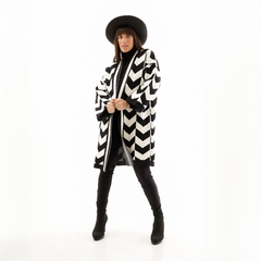 Modelo luciendo un saco de diseño en zigzag en blanco y negro, con sombrero negro y pantalones ajustados.